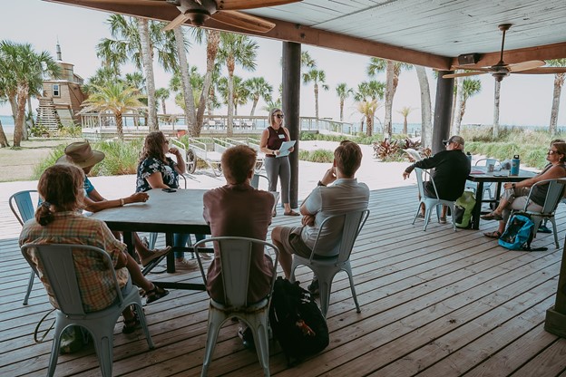 Person speaking to people sitting at tables in an outdoor pavillion